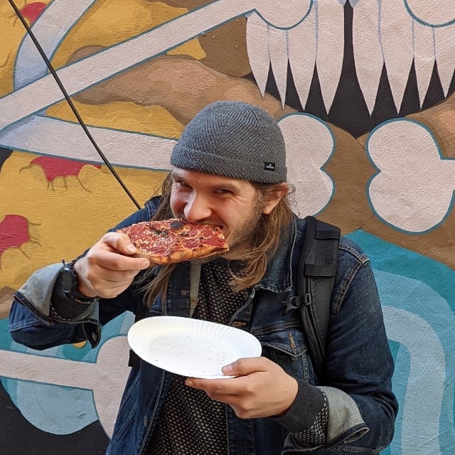 Photo of Brett eating a slice of vegan pizza